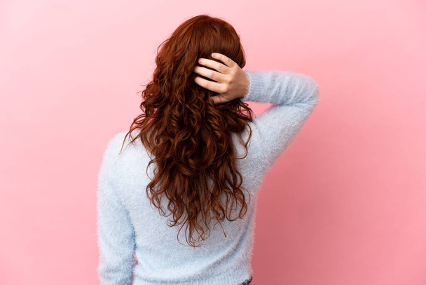 tiener roodachtig vrouw geïsoleerd op roze achtergrond in rug positie en denken - Foto, afbeelding