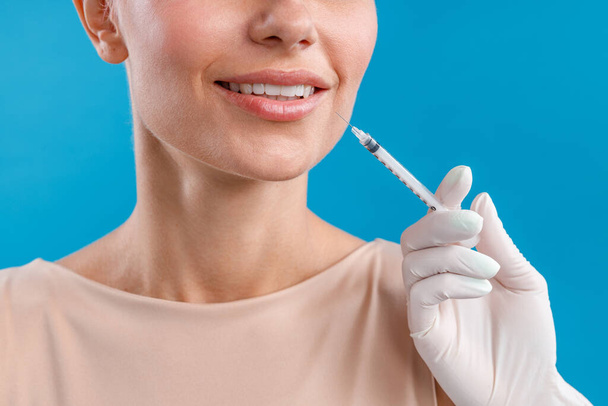 Close up shot of smiling woman receiving botox injection in lips from beautician - 写真・画像