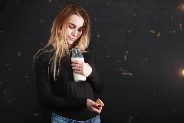 Young girl drinks milk from a bottle on a black wall background - Valokuva, kuva