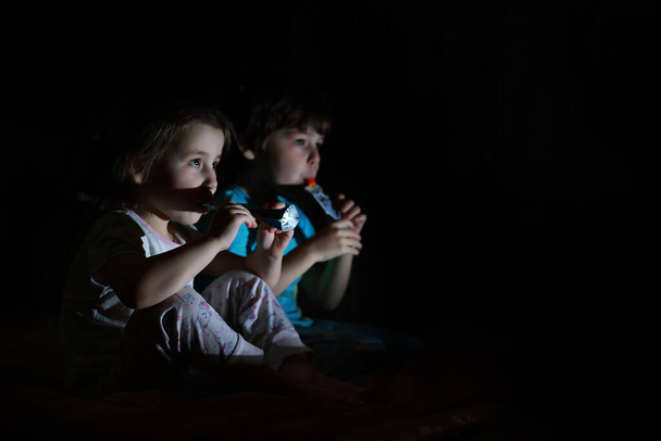 Küçük çocuklar karanlık bir odada gece televizyon izliyorlar. - Fotoğraf, Görsel