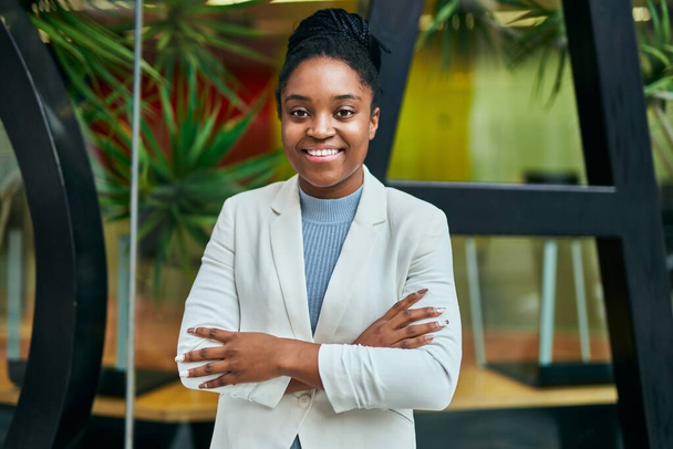 Νεαρή Αφροαμερικανή επιχειρηματίας χαμογελά ευτυχισμένη με σταυρωμένα τα χέρια στην πόλη. - Φωτογραφία, εικόνα