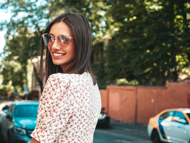 Young beautiful smiling hipster woman in trendy summer dress. Sexy carefree woman posing on the street background at sunset. Positive model outdoors  in sunglasses. Cheerful and happy  - Valokuva, kuva