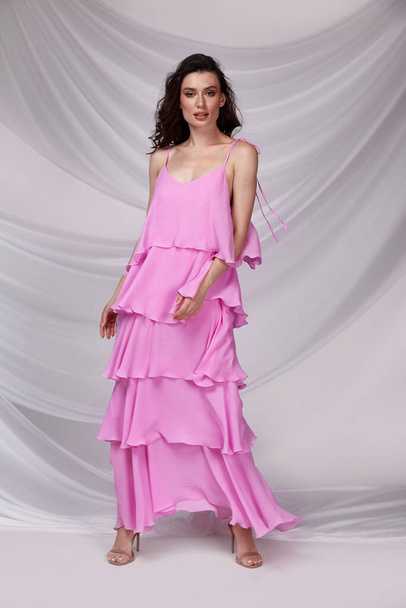 Krásná sexy žena nosit světlo dlouhé růžové barvy šaty letní kolekce bavlna ležérní styl opálené tělo bruneta vlasy krásná tvář make-up bílý pozadí studio. - Fotografie, Obrázek