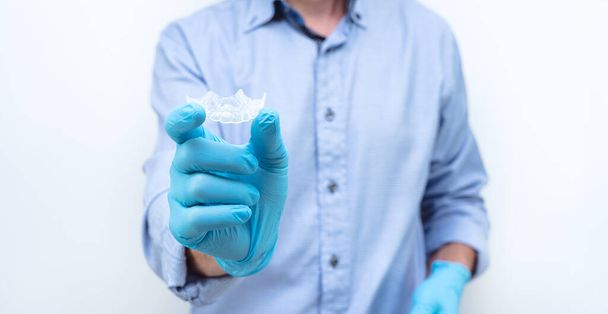 Dentist in gloves and blue shirt showing a clear dental splint. Copy space. - Фото, изображение
