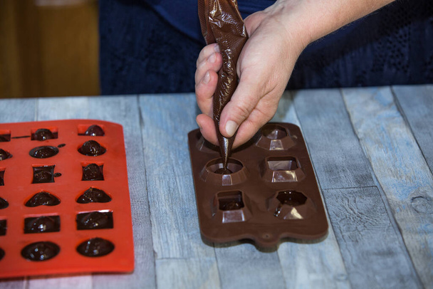 Step-by-step process of making chocolates from dark chocolate and cherries in cognac at home. A woman pours hot chocolate into candy molds with prepared cherries. Culinary blog concept. - Photo, image