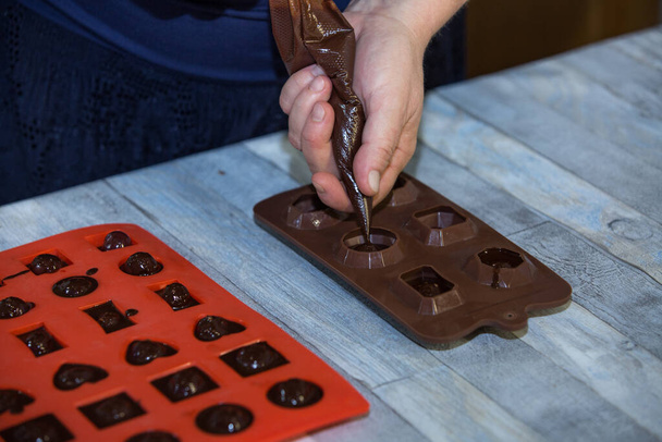 Vaiheittainen prosessi, jossa tehdään suklaata tummasta suklaasta ja kirsikoita konjakissa kotona. Nainen kaataa kuumaa kaakaota makeismuotteihin valmistettujen kirsikoiden kanssa. Kulinaarinen blogi käsite. - Valokuva, kuva