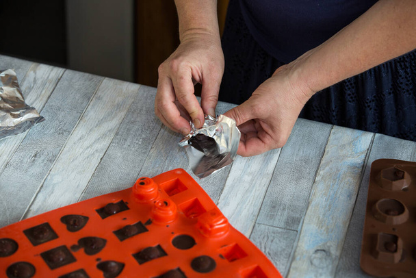 Schritt für Schritt werden zu Hause Pralinen aus dunkler Schokolade und Kirschen in Cognac hergestellt. Jedes Bonbon wird aus der Silikonform entfernt und in Folie gewickelt. Kulinarisches Blog-Konzept. - Foto, Bild