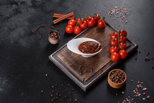 Red sauce or ketchup in a bowl and ingredients for cooking, spices, garlic, tomatoes and herbs on a black background - Fotoğraf, Görsel