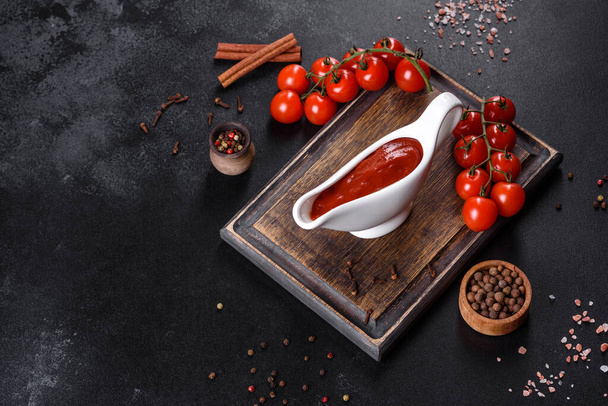 Piros szósz vagy ketchup tálban és összetevők főzéshez, fűszerekhez, fokhagymához, paradicsomhoz és fűszernövényekhez fekete alapon - Fotó, kép