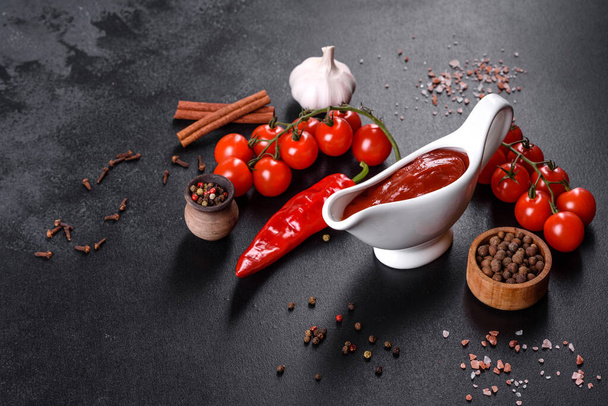 Red sauce or ketchup in a bowl and ingredients for cooking, spices, garlic, tomatoes and herbs on a black background - Foto, afbeelding