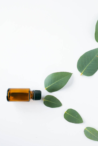 A closeup shot of 1ml amber essential oil vial and green leaves isolated on a white background - Foto, afbeelding