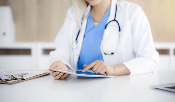 Unknown woman-doctor sitting in sunny clinic and using tablet pc, close-up. Data and best service in medicine - Photo, Image