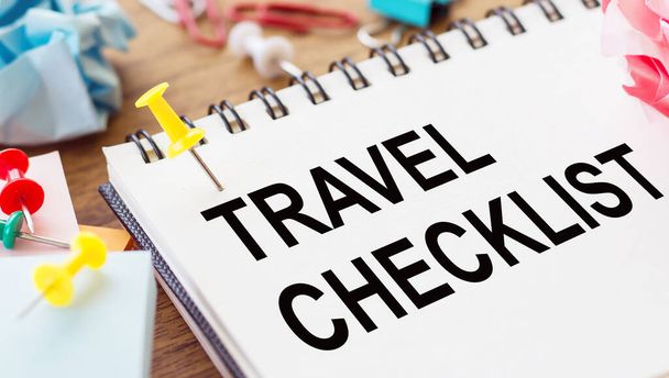 TRAVEL CHECKLIST - text on a notepad with wrinkled paper and paper needles on wooden background. - Foto, Imagen
