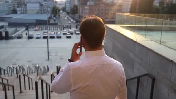 Unenomainen komea liikemies juo kahvia lähellä rakennusta ja soittaa - Materiaali, video