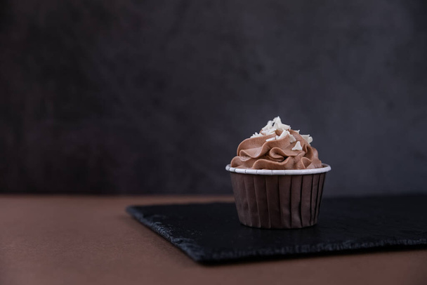 Delicious chocolate cupcake with cream and white chocolate sprinkling on a dark background. Sweets for a party - Foto, Bild