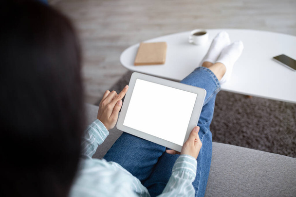 Kanepede oturan tanınmayan Hintli kadın evde boş ekranlı tablet kullanıyor. Uygulama veya web sitesi için maket yapıyor. - Fotoğraf, Görsel