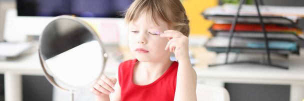 Little girl paints her eyes and looks in mirror - Foto, imagen