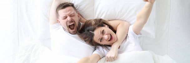 Yawning happy man and woman lie on large white bed - Photo, Image