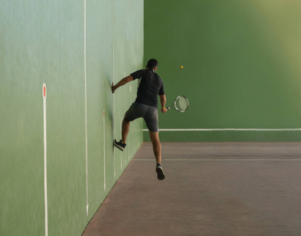 giovane ragazzo che salta oltre il muro su un campo di fronton mentre utilizza la racchetta da tennis per segnare un punto nella partita con attenzione selettiva. - Foto, immagini