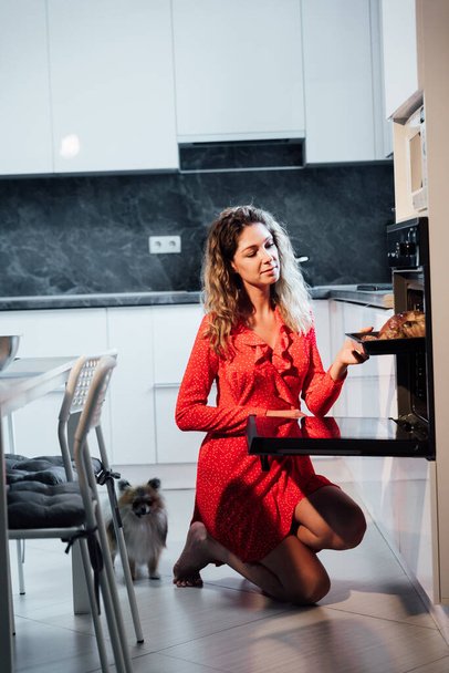mooie vrouw huisvrouw kookt kip in de oven in de keuken - Foto, afbeelding