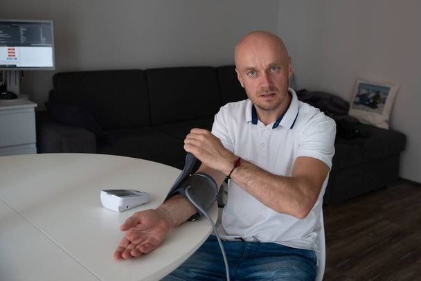 Muž pomocí domácí krevní tlak stroj zkontrolovat své zdraví sedí v obývacím pokoji - Fotografie, Obrázek