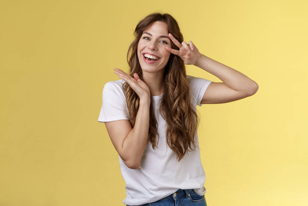 Lively enthusiastic attractive carefree woman enjoy relaxed weekends summer holiday have fun smiling broadly tilt head show peace victory sign joyfully introduce herself posing yellow background - Photo, Image