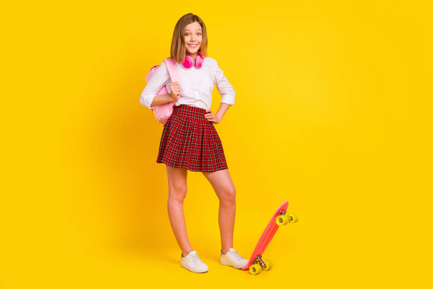 Full length photo of little girl with skate headphones wear shirt skirt bag sneakers isolated on yellow background - 写真・画像
