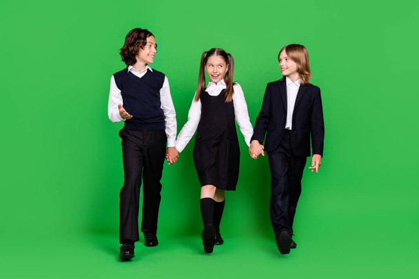 Full body photo of funny small girl boys hold hands go wear school uniform isolated on green background - Fotoğraf, Görsel