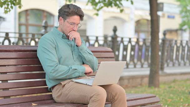 Mature Adult Man Feeling Angry while using Laptop on Bench  - 写真・画像