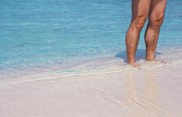 Un hombre se encuentra en la cálida playa de arena frente al mar azul - Foto, Imagen