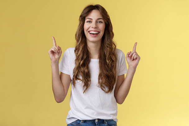 Charismatic enthusiastic attractive lively woman having fun enjoy awesome night out party laughing joyfully pointing up index fingers up introduce promo smiling happily yellow background - Photo, Image