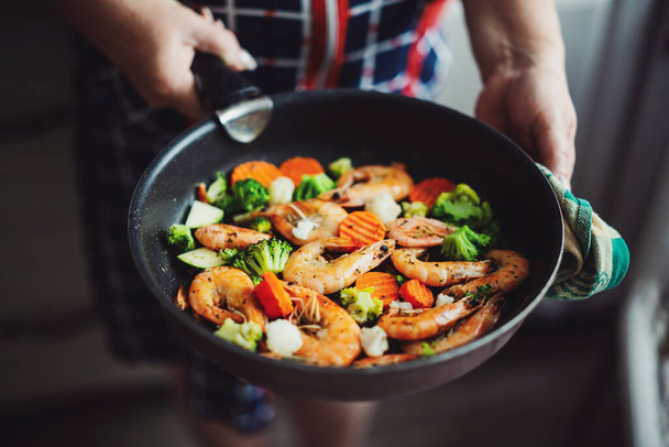 Woman staying at home kitchen and cooking shrimps with vegetables on pan. Home cooking or healthy cooking concept - Fotó, kép