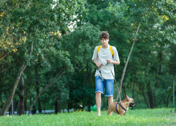 公園でかわいい赤いフランスのブルドッグと一緒に歩いている10代。犬との友情の中で - 写真・画像