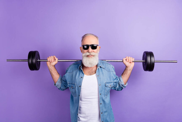 Photo of aged sporty man training intense muscles arms barbell isolated over violet color background - Φωτογραφία, εικόνα