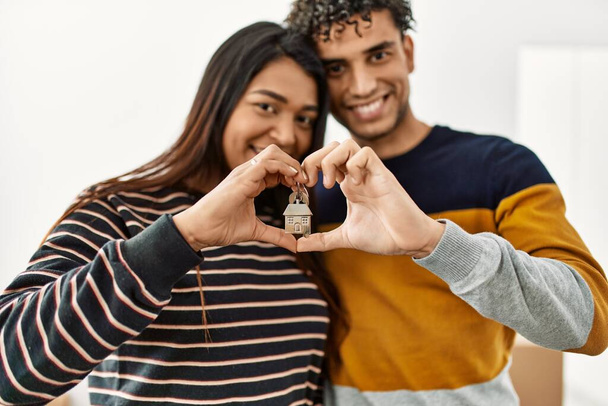 Jeune couple latin faisant symbole de coeur avec les mains tenant la clé de la nouvelle maison. - Photo, image