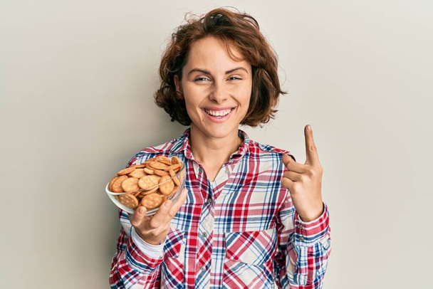 Genç esmer kadın elinde tuzlu bisküvilerle gülümsüyor bir fikirle ya da soru işareti ile mutlu bir yüzle, bir numara  - Fotoğraf, Görsel