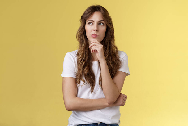 Thoughtful smart creative female freelancer trying solve puzzle making choice pondering decision touch chin thinking look away focused thinking deep stand yellow background - Foto, afbeelding