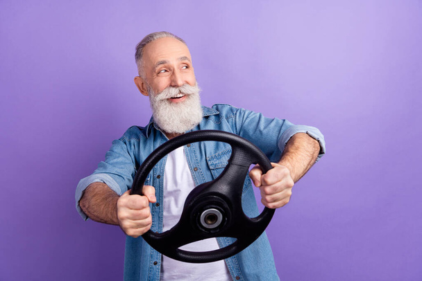 Photo of aged man happy positive smile ride car look empty space hold steering-wheel isolated over violet color background - Photo, Image