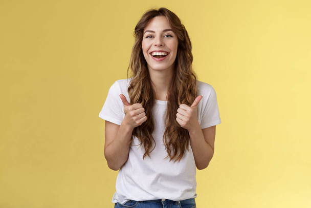 Pleased outgoing cheerful good-looking caucasian girl curly long haircut white t-shirt show thumbs up smiling lively pleased like awesome performance approve good choice yellow background - Photo, Image