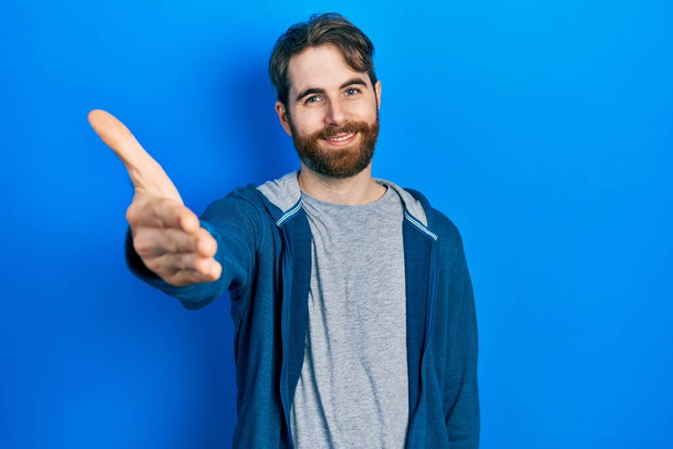 Kaukasischer Mann mit Bart in lässigem Sweatshirt, freundlich lächelnd und per Handschlag zur Begrüßung. Erfolgreiches Geschäft.  - Foto, Bild