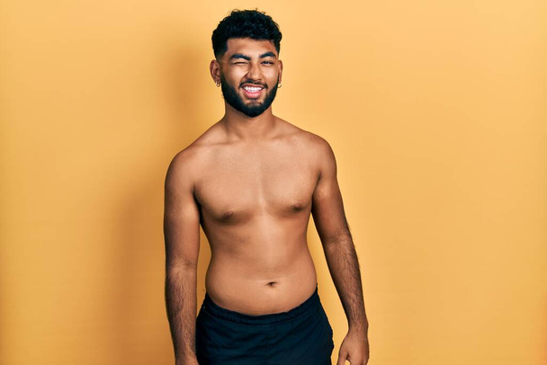 Arab man with beard wearing swimwear shirtless winking looking at the camera with sexy expression, cheerful and happy face.  - Valokuva, kuva