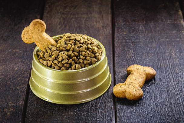 корм для собак с костяной формой печенья в золотой миске на деревянном фоне, пространство для копирования - Фото, изображение