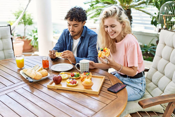 Молодая пара улыбается счастливый завтрак, сидя на столе на террасе. - Фото, изображение