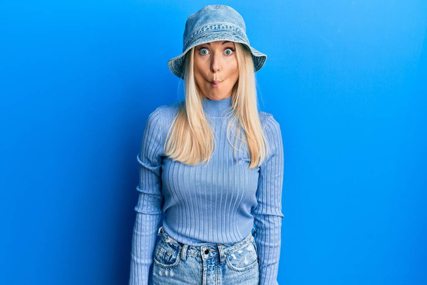 Young blonde woman wearing casual denim hat making fish face with lips, crazy and comical gesture. funny expression.  - Photo, Image