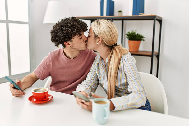 Young couple using smartphone and drinking coffee at home. - Photo, Image