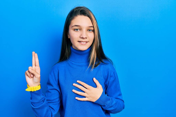 Mladá brunetka dívka na sobě rolák svetr s úsměvem nadávky s rukou na hrudi a prsty nahoru, dávat věrnostní slib  - Fotografie, Obrázek