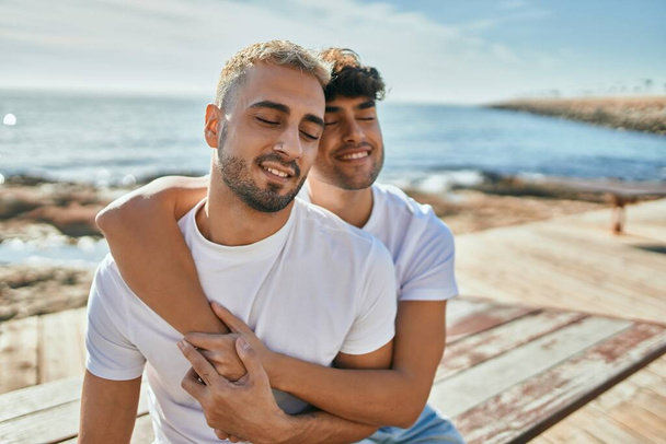 Молода гей-пара посміхається щасливий сидячи на лавці на березі набережної
. - Фото, зображення