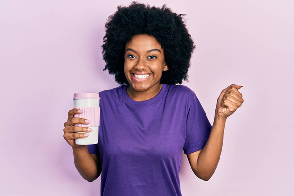 アフリカ系アメリカ人の若い女性は誇りを持って叫んでコーヒーを保持します,勝利と成功を祝う非常に腕を上げ興奮  - 写真・画像