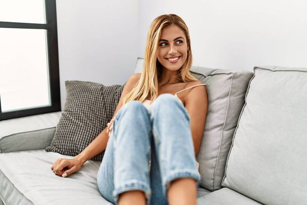 Молода біла дівчина посміхається щасливо сидячи на дивані вдома
. - Фото, зображення
