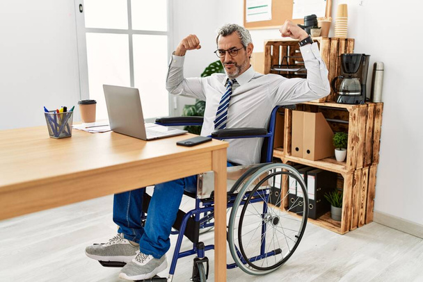 Latynos w średnim wieku, pracujący w biurze, siedzący na wózku inwalidzkim, z dumnymi mięśniami rąk. koncepcja sprawności.  - Zdjęcie, obraz